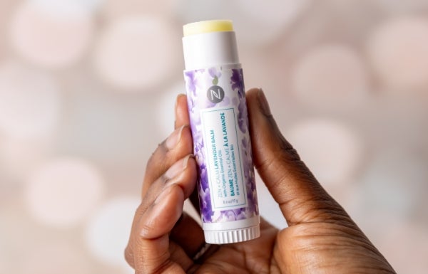 A woman holding up the Zen + Calm Lavender Balm to her ear.